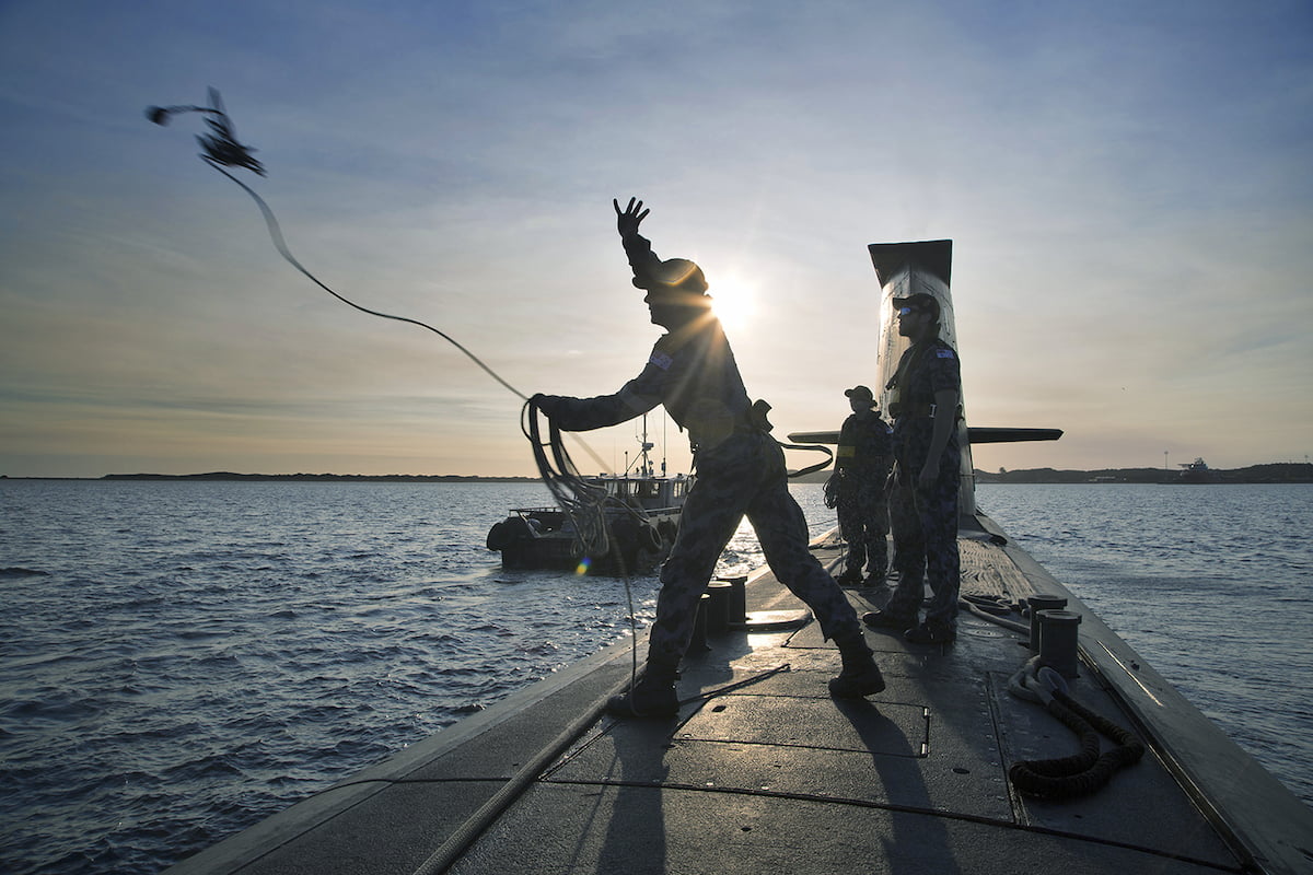 Members of the Navy standing on top of a submarine throwing a rope.