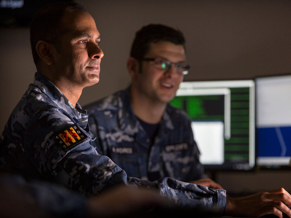 Two members of the Air force are working in an office surrounded by computer screens.