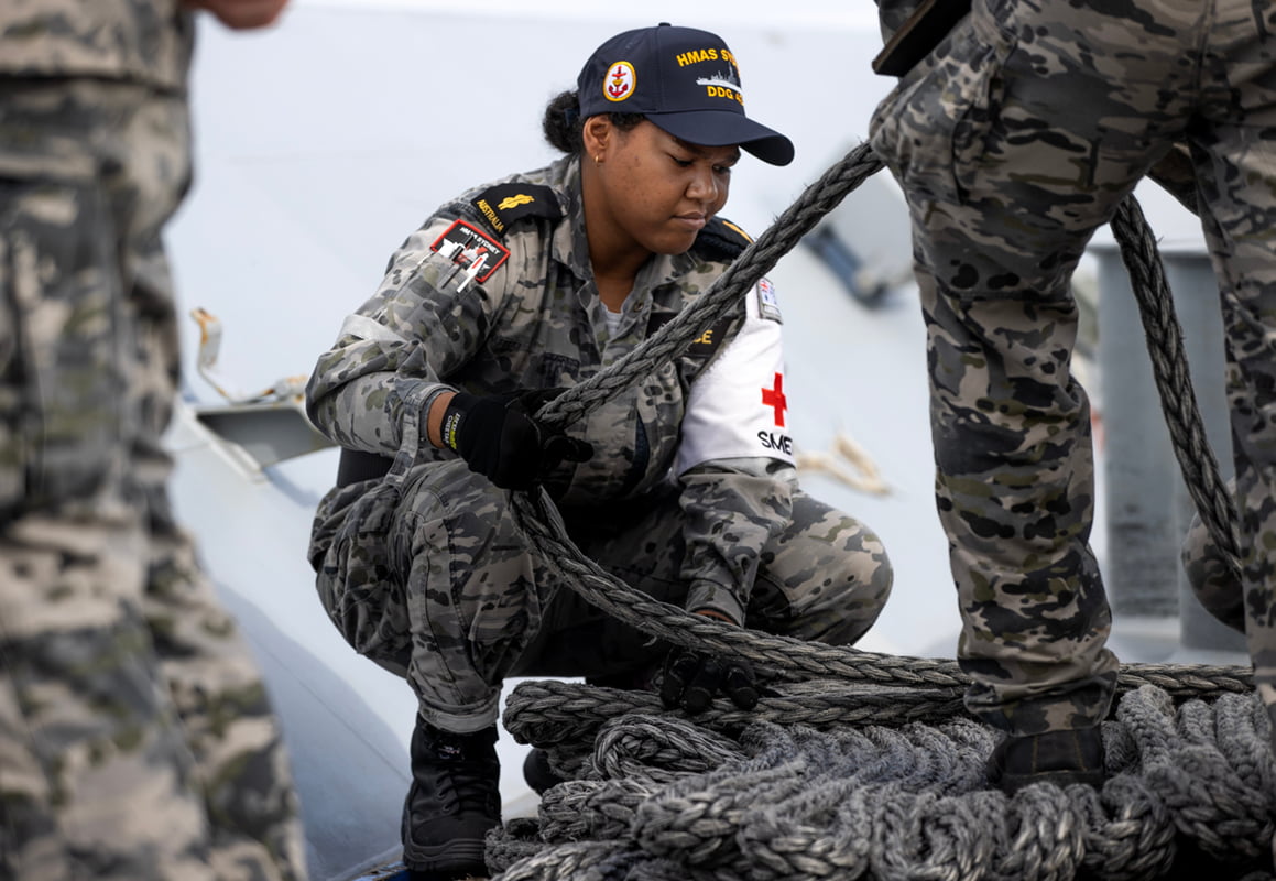 A member of the Navy on a ship tying a rope securely.